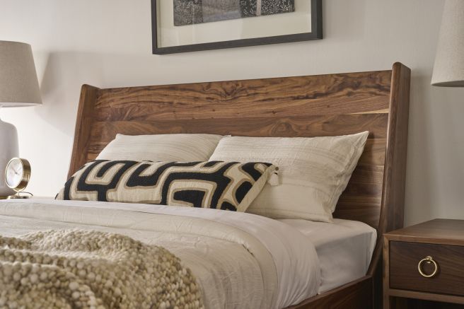 Detail of a hardwood bed headboard showing natural walnut patterning behind layered cream pillows.