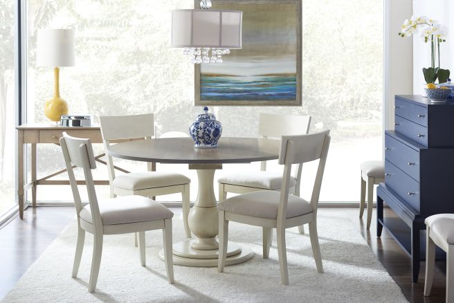 Stylish dining room with upholstered dining chairs surrounding a round pedestal table, complemented by a navy blue chest and bright decor accents.