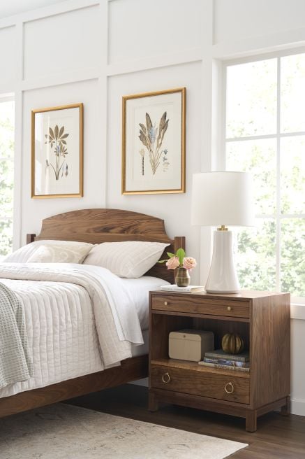 Walnut wood bed and nightstand in a bright bedroom with floral artwork and natural light.