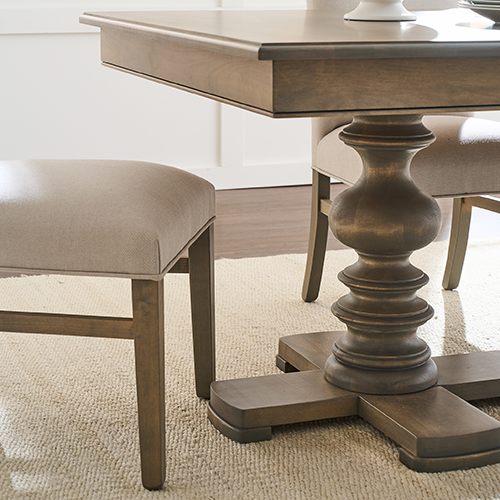 Close-up of a solid wood dining table with a sculpted pedestal base and a rich, warm finish.